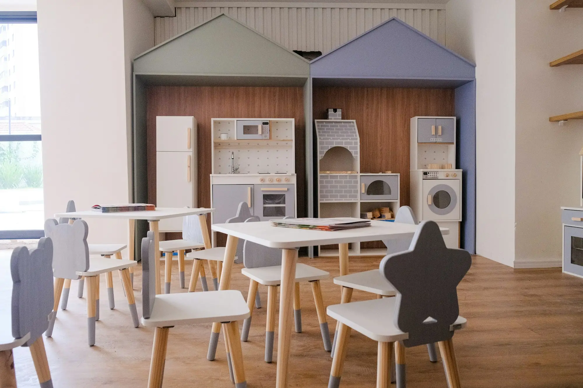 Helle Spielecke im Wartezimmer mit kleinen Tischen, Stühlen und Regalen in Hausform.