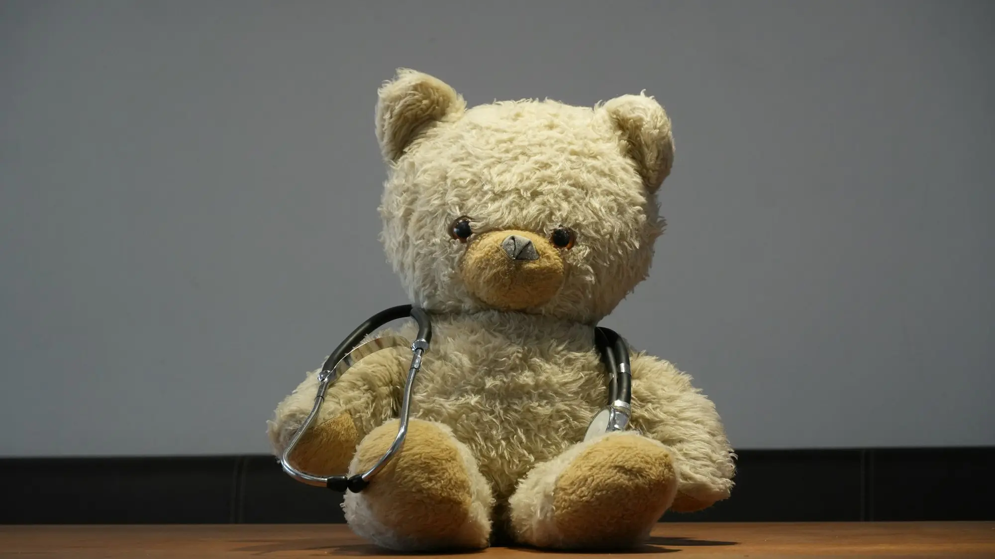 Ein Teddybär mit Stethoskop sitzt auf einem Tisch.